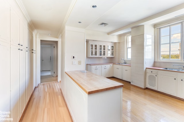 kitchen featuring white cabinets, butcher block countertops, light hardwood / wood-style floors, and sink