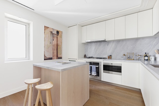 kitchen with white cabinets, light wood-type flooring, appliances with stainless steel finishes, and tasteful backsplash