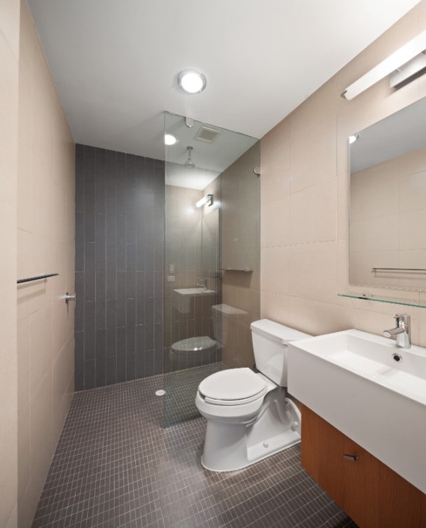 bathroom featuring tile patterned floors, a tile shower, vanity, tile walls, and toilet