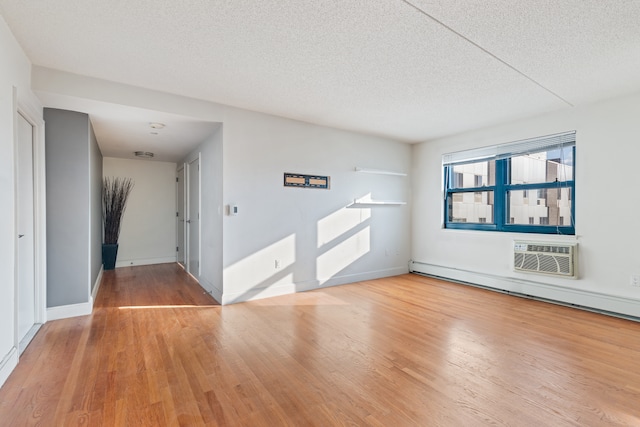 spare room featuring hardwood / wood-style flooring, an AC wall unit, a textured ceiling, and a baseboard radiator