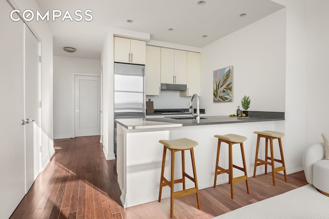 kitchen with dark hardwood / wood-style floors, kitchen peninsula, sink, and high end refrigerator