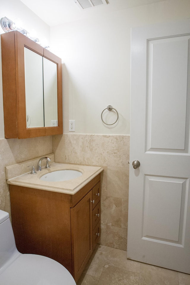 bathroom featuring vanity, toilet, and tile walls