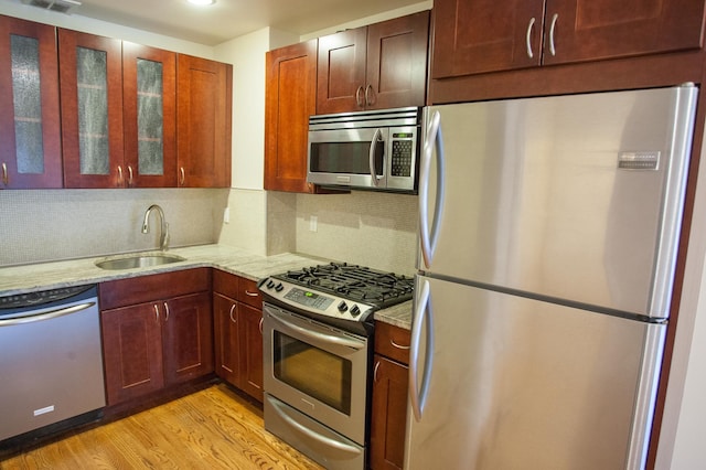 kitchen with light stone countertops, sink, stainless steel appliances, tasteful backsplash, and light wood-type flooring