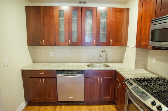 kitchen with backsplash, stainless steel appliances, light stone counters, and sink