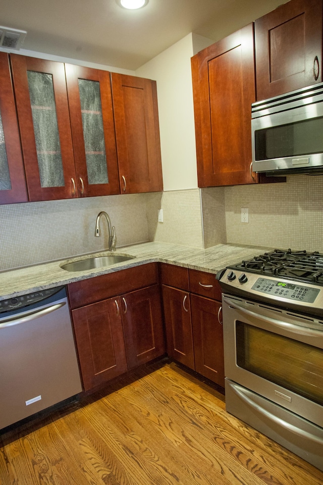 kitchen with sink, light stone countertops, tasteful backsplash, light hardwood / wood-style floors, and stainless steel appliances