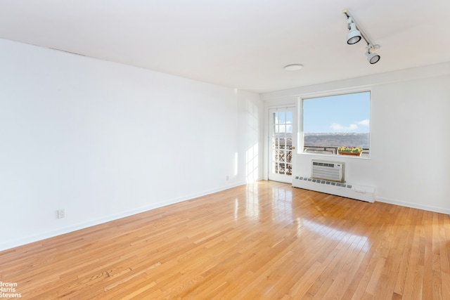 unfurnished living room featuring a wall unit AC, rail lighting, a baseboard heating unit, and light wood-type flooring