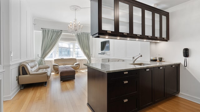 bar with sink, light stone counters, light hardwood / wood-style flooring, crown molding, and decorative light fixtures