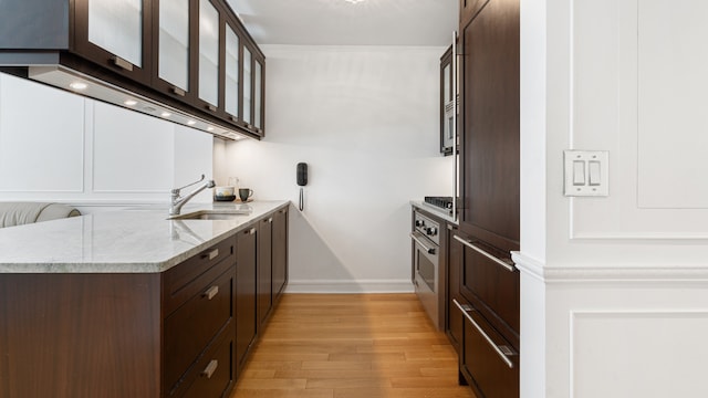 kitchen featuring dark brown cabinets, light stone counters, sink, and light hardwood / wood-style flooring