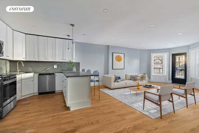 kitchen with white cabinetry, backsplash, kitchen peninsula, appliances with stainless steel finishes, and light wood-type flooring