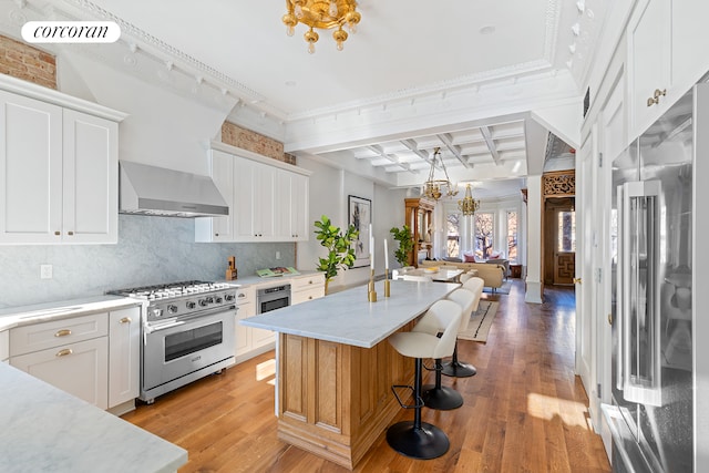 kitchen featuring a center island, coffered ceiling, wall chimney exhaust hood, premium appliances, and white cabinetry