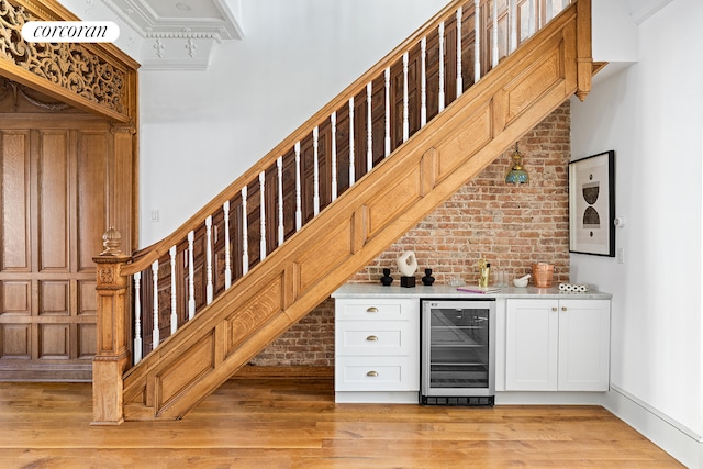 bar featuring white cabinetry, wine cooler, brick wall, light hardwood / wood-style floors, and ornamental molding