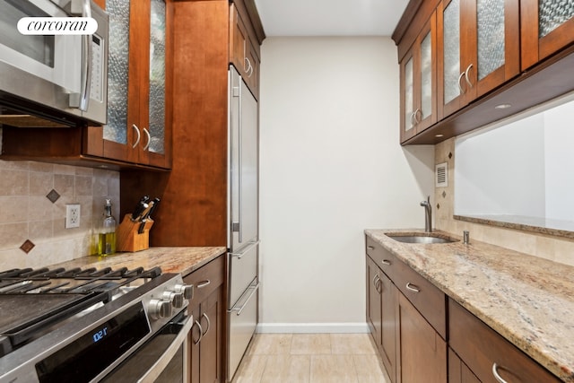 kitchen featuring high quality appliances, sink, light stone countertops, light tile patterned floors, and tasteful backsplash