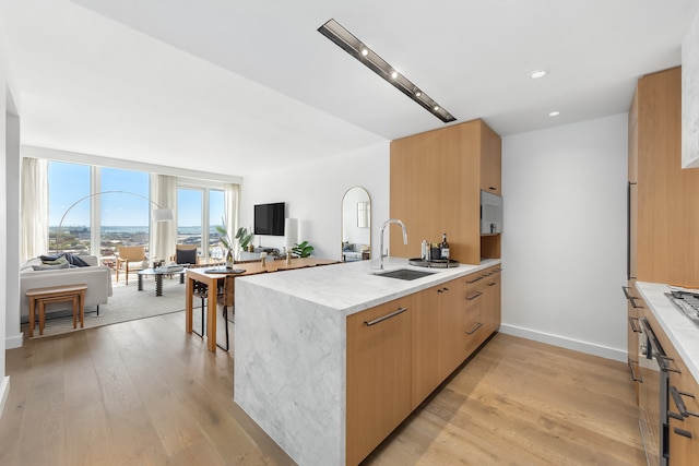 kitchen with light stone countertops, sink, light brown cabinets, kitchen peninsula, and light hardwood / wood-style floors