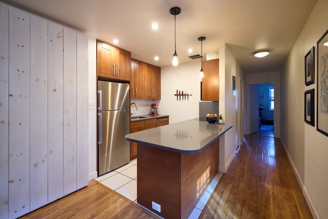 kitchen featuring sink, kitchen peninsula, stainless steel fridge, light hardwood / wood-style floors, and decorative light fixtures