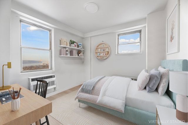 bedroom with a wall mounted AC, multiple windows, and light wood-type flooring