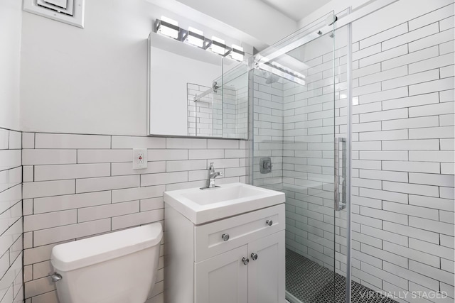 bathroom featuring vanity, toilet, a shower with shower door, and tile walls