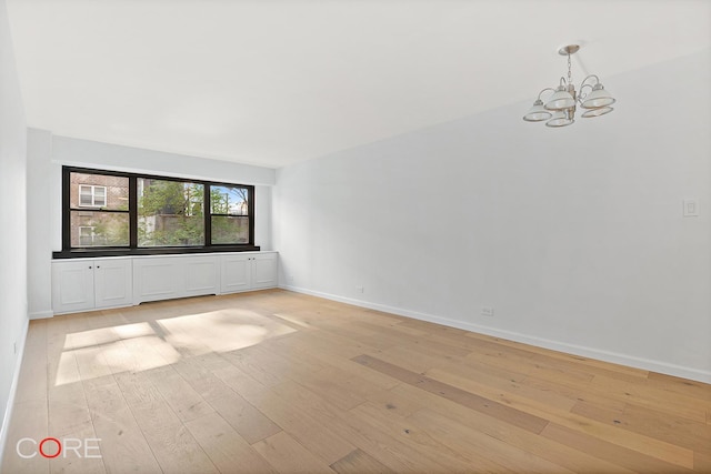 spare room featuring light wood-type flooring and a chandelier