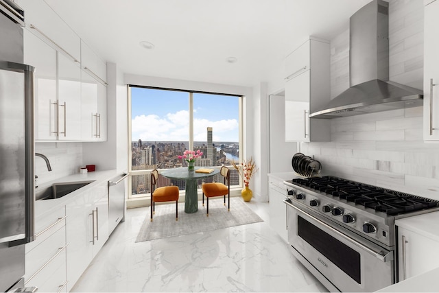 kitchen featuring white cabinets, wall chimney range hood, sink, decorative backsplash, and appliances with stainless steel finishes