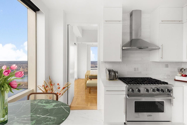 kitchen with high end range, backsplash, white cabinets, and wall chimney range hood