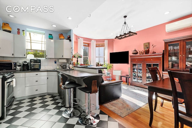 kitchen featuring white cabinets, a wealth of natural light, a wall mounted AC, decorative light fixtures, and stainless steel range with gas stovetop