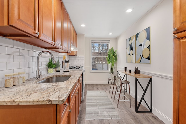 kitchen featuring light stone countertops, sink, light hardwood / wood-style flooring, decorative backsplash, and stainless steel range with gas stovetop