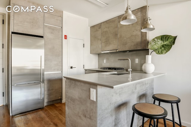 kitchen featuring dark wood-type flooring, kitchen peninsula, stainless steel fridge, decorative backsplash, and a breakfast bar