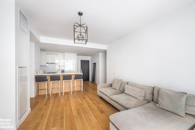 living room with light hardwood / wood-style floors, sink, and an inviting chandelier