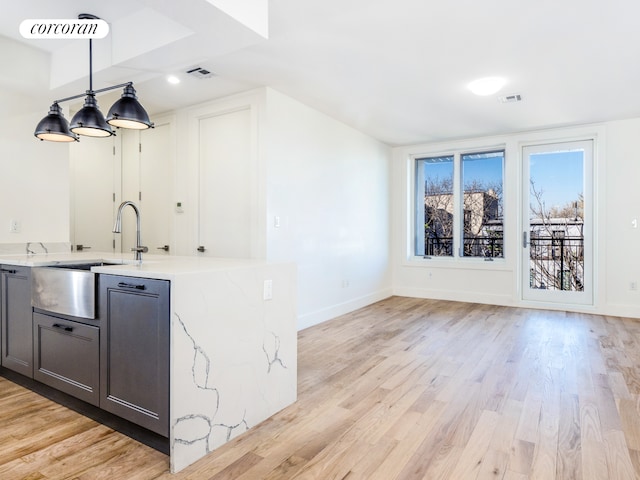 bar featuring light stone counters, sink, pendant lighting, and light wood-type flooring