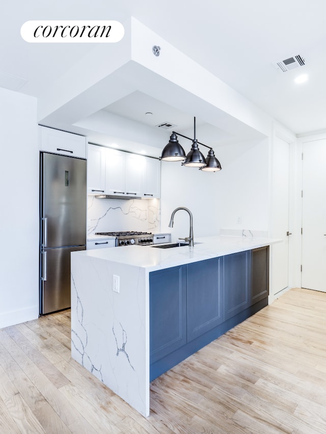 kitchen featuring stainless steel fridge, backsplash, light wood-type flooring, decorative light fixtures, and white cabinets