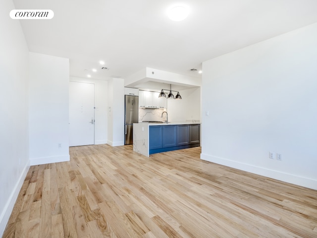 interior space with decorative backsplash, blue cabinets, pendant lighting, light hardwood / wood-style flooring, and stainless steel refrigerator