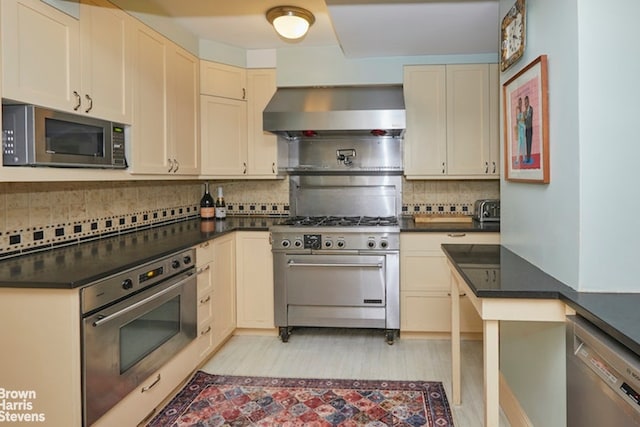 kitchen featuring cream cabinetry, appliances with stainless steel finishes, backsplash, and wall chimney range hood