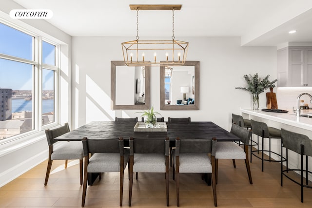 dining space with a chandelier, light wood-type flooring, a water view, and sink