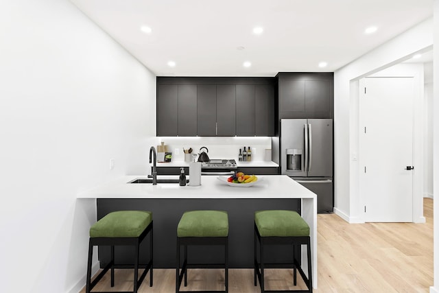 kitchen featuring kitchen peninsula, appliances with stainless steel finishes, light wood-type flooring, a breakfast bar, and sink