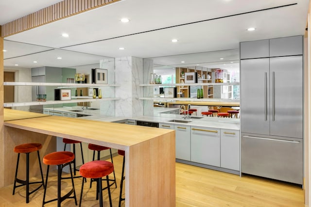 kitchen with sink, a kitchen breakfast bar, light hardwood / wood-style flooring, kitchen peninsula, and stainless steel built in fridge