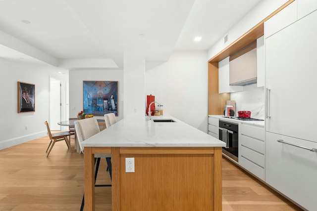 kitchen featuring sink, stainless steel appliances, a kitchen island with sink, white cabinets, and light wood-type flooring