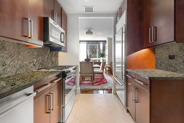 kitchen with light tile patterned flooring, dark stone countertops, appliances with stainless steel finishes, and tasteful backsplash