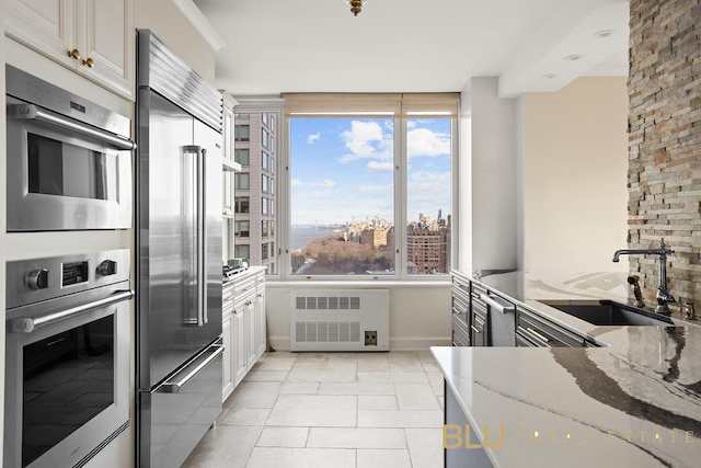 kitchen featuring light stone countertops, appliances with stainless steel finishes, sink, white cabinets, and radiator heating unit