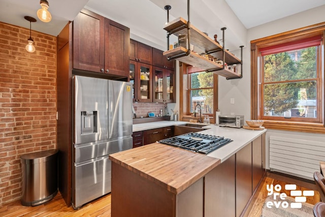 kitchen featuring sink, stainless steel appliances, brick wall, decorative light fixtures, and light wood-type flooring