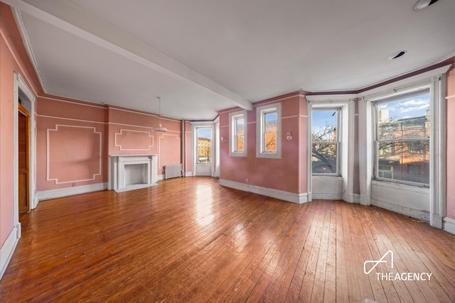 unfurnished living room with beamed ceiling, wood-type flooring, ornamental molding, and radiator