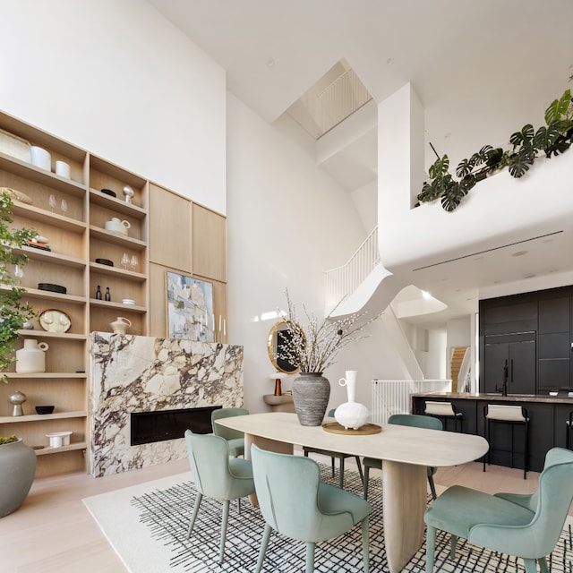 dining space featuring a high end fireplace, a towering ceiling, and light hardwood / wood-style floors