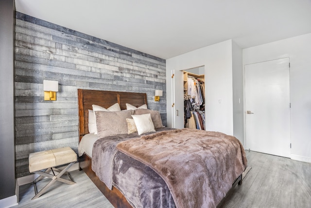 bedroom featuring hardwood / wood-style floors, a walk in closet, wooden walls, and a closet