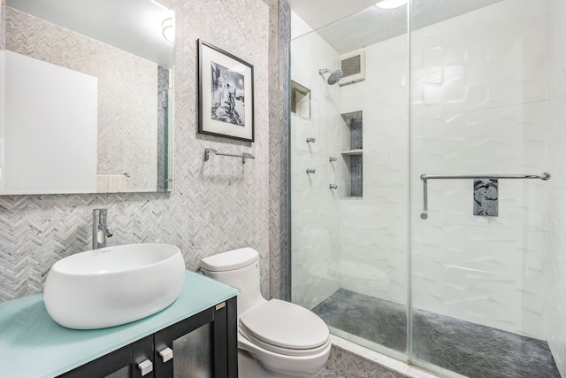 bathroom featuring toilet, decorative backsplash, vanity, a shower with shower door, and tile walls