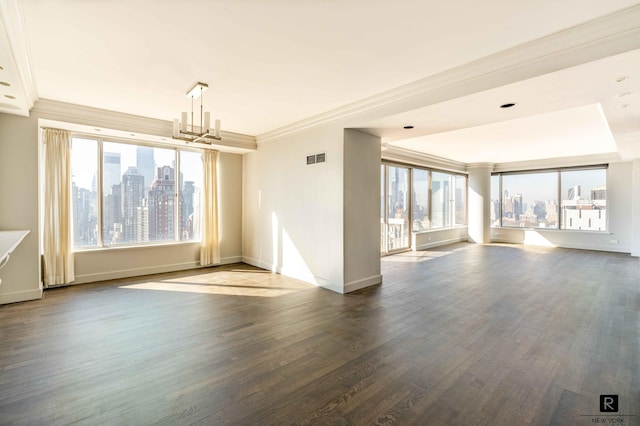 empty room with a healthy amount of sunlight, dark hardwood / wood-style flooring, crown molding, and an inviting chandelier