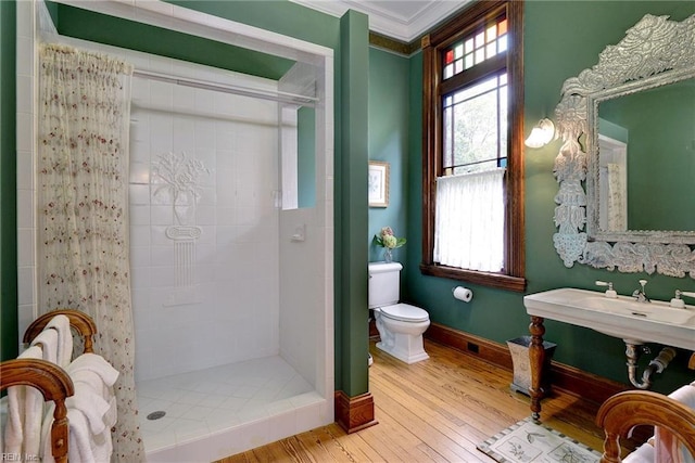 bathroom with crown molding, toilet, hardwood / wood-style flooring, and a tile shower