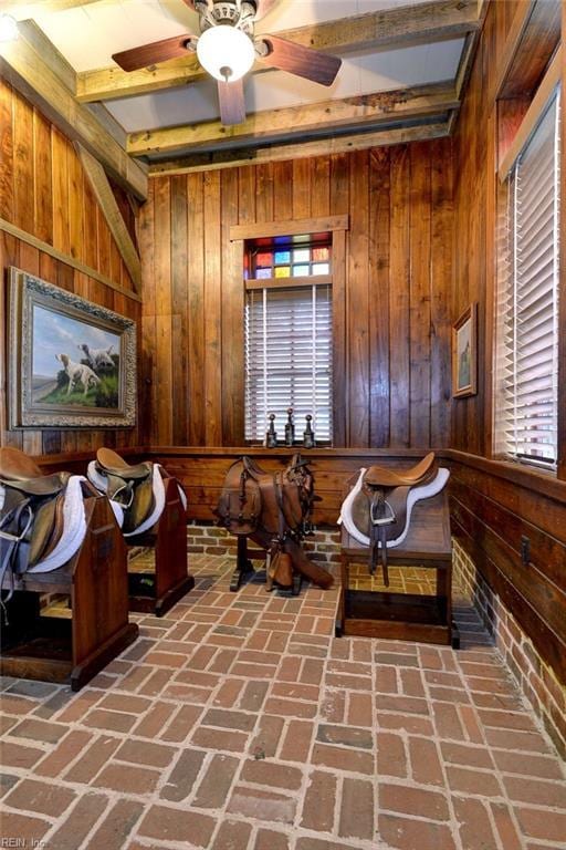 sitting room featuring wood walls, ceiling fan, and beamed ceiling