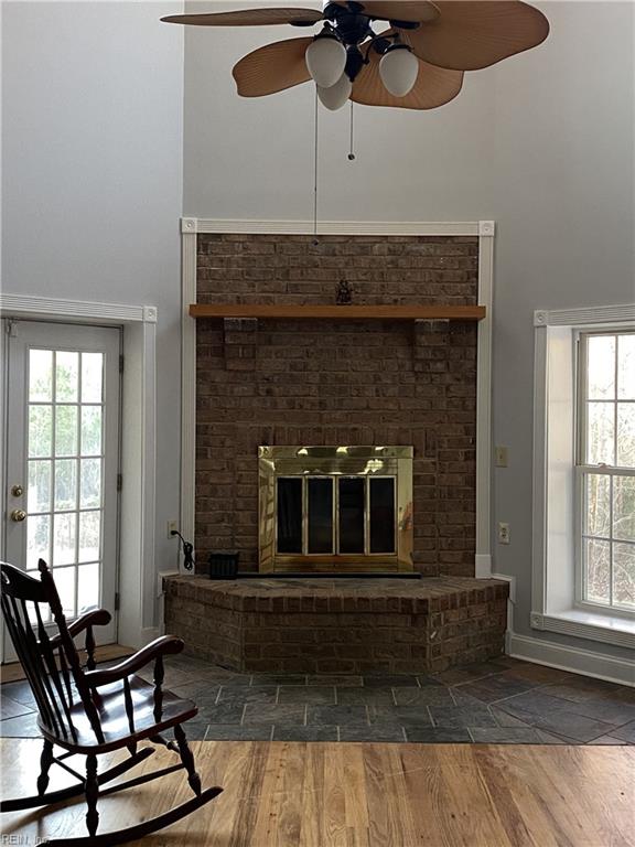 living room with ceiling fan, a brick fireplace, and dark wood-type flooring