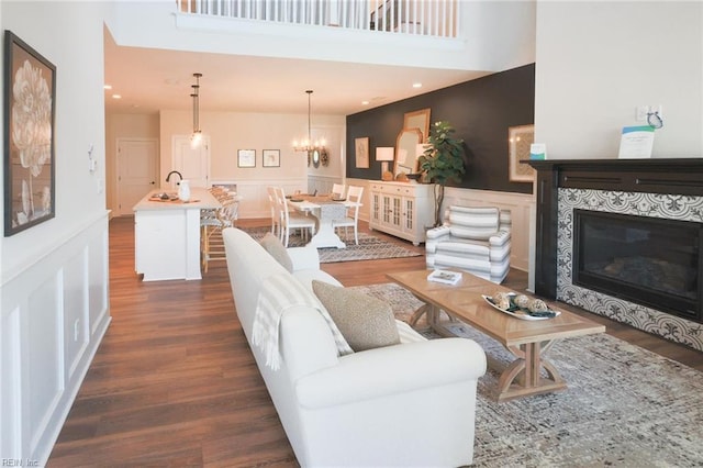 living room with dark wood-type flooring, a tiled fireplace, a high ceiling, and an inviting chandelier