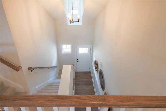 stairs with dark wood-type flooring, a towering ceiling, and a notable chandelier