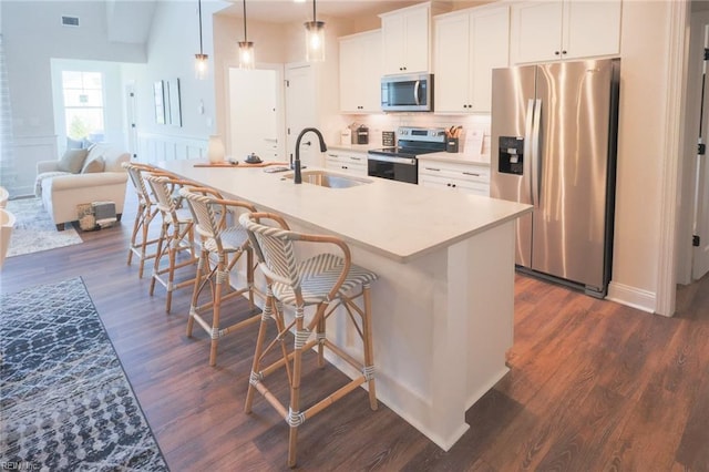 kitchen with white cabinets, dark wood-type flooring, a kitchen island with sink, stainless steel appliances, and sink