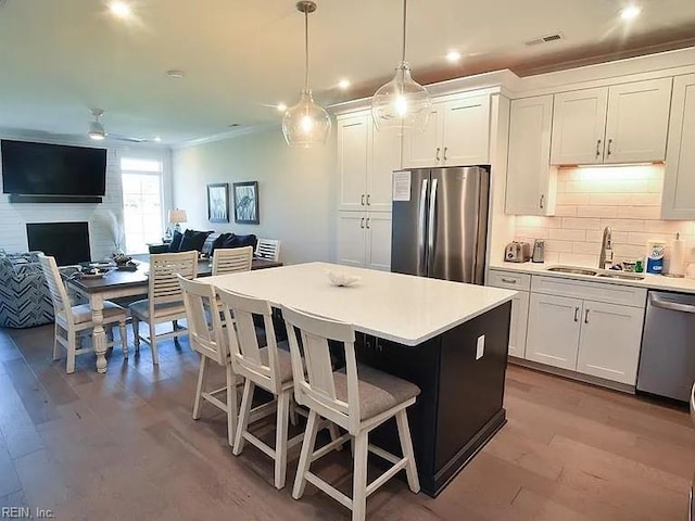 kitchen with appliances with stainless steel finishes, sink, decorative light fixtures, light hardwood / wood-style floors, and white cabinetry